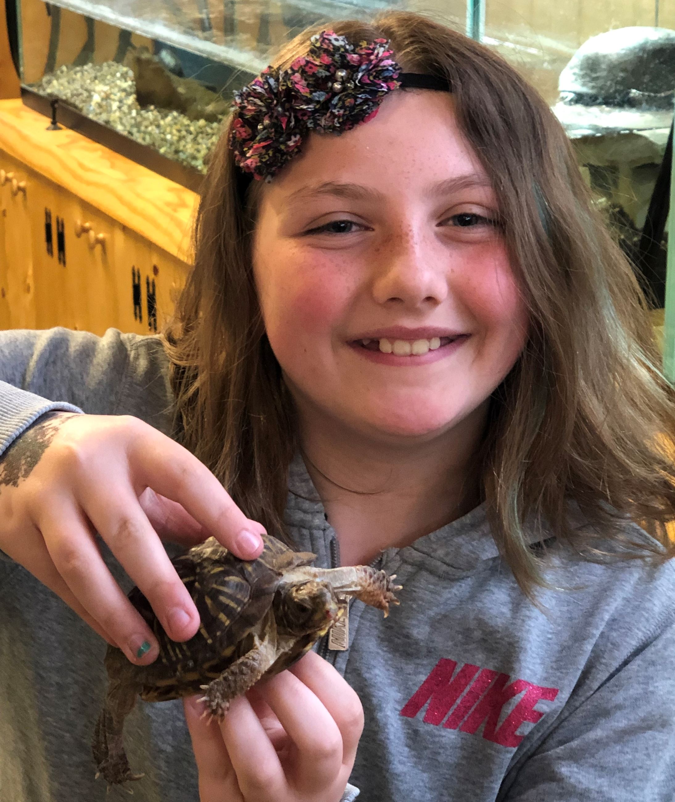 A girl holding a box turtle. She is smiling.